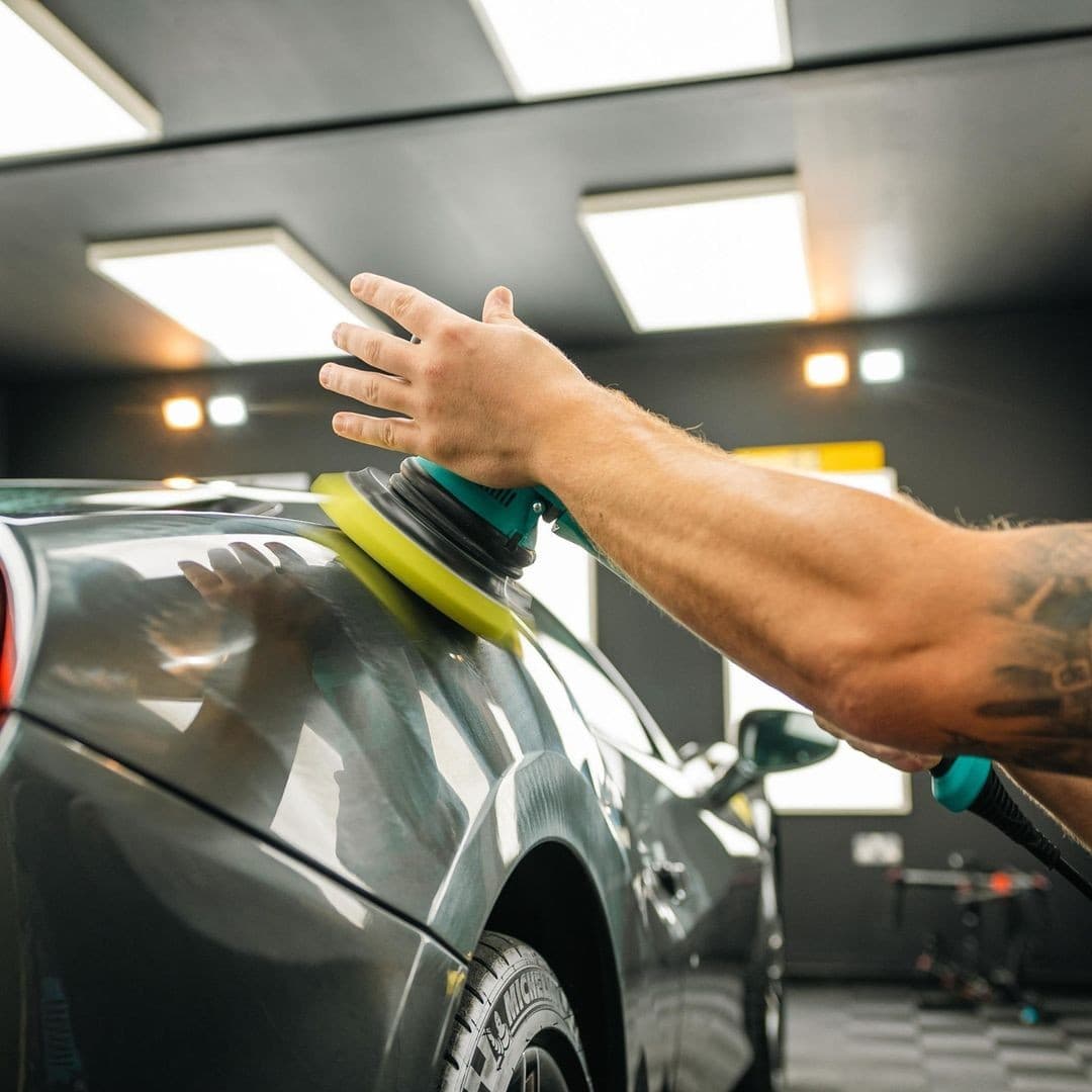 A detailer machine polishing a car’s bodywork with a dual-action polisher