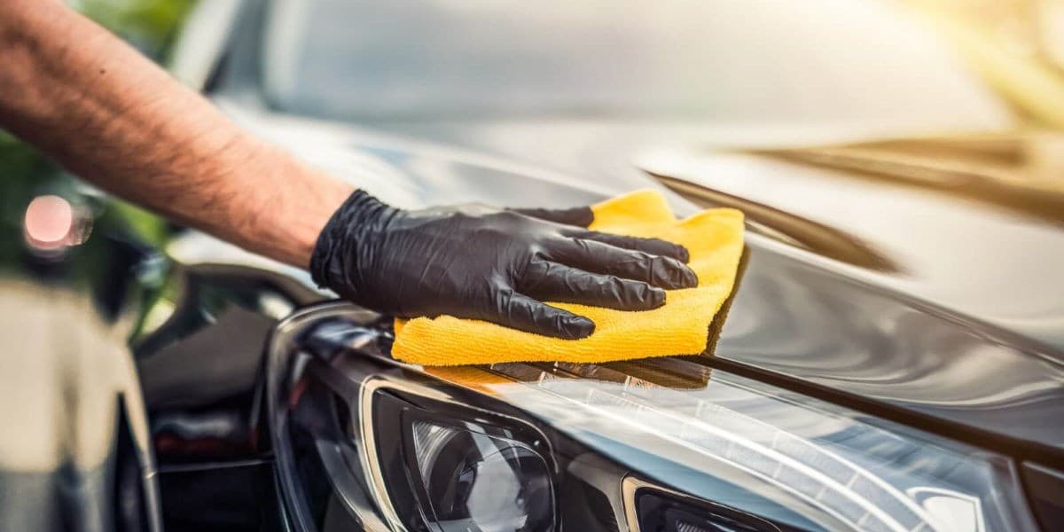 A gloved hand wiping a car’s headlight with a yellow microfibre cloth